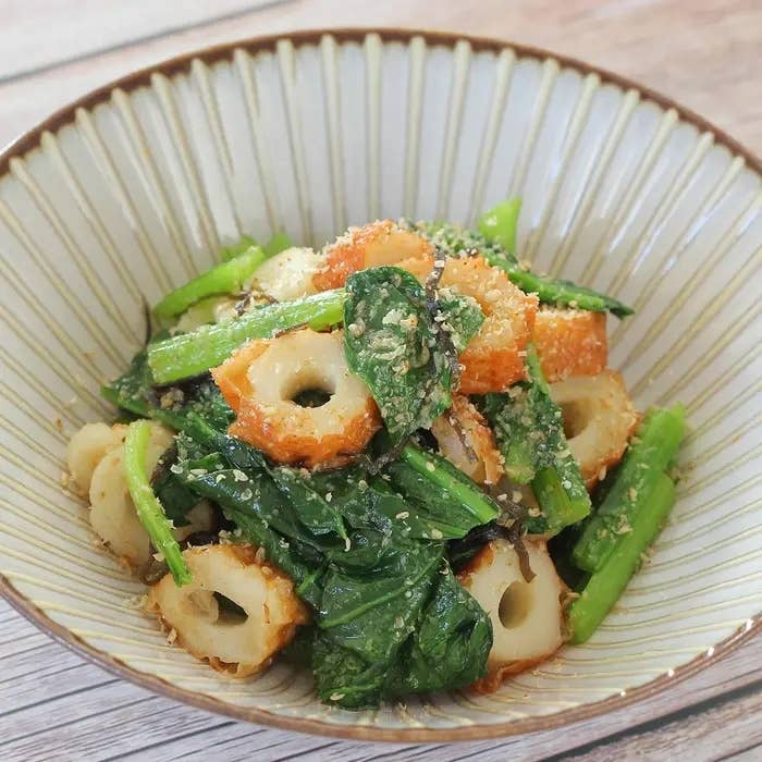 和風サラダがボウルに盛られており、ちくわと緑の葉物野菜が含まれている。香ばしいごまが振りかけられている。