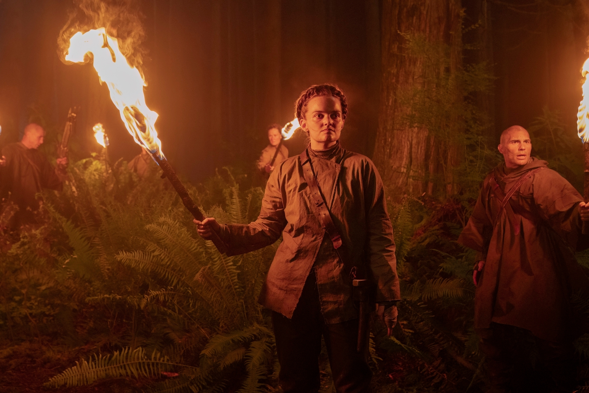 Grupo de personas en un bosque oscuro sosteniendo antorchas, creando una atmósfera intensa y misteriosa