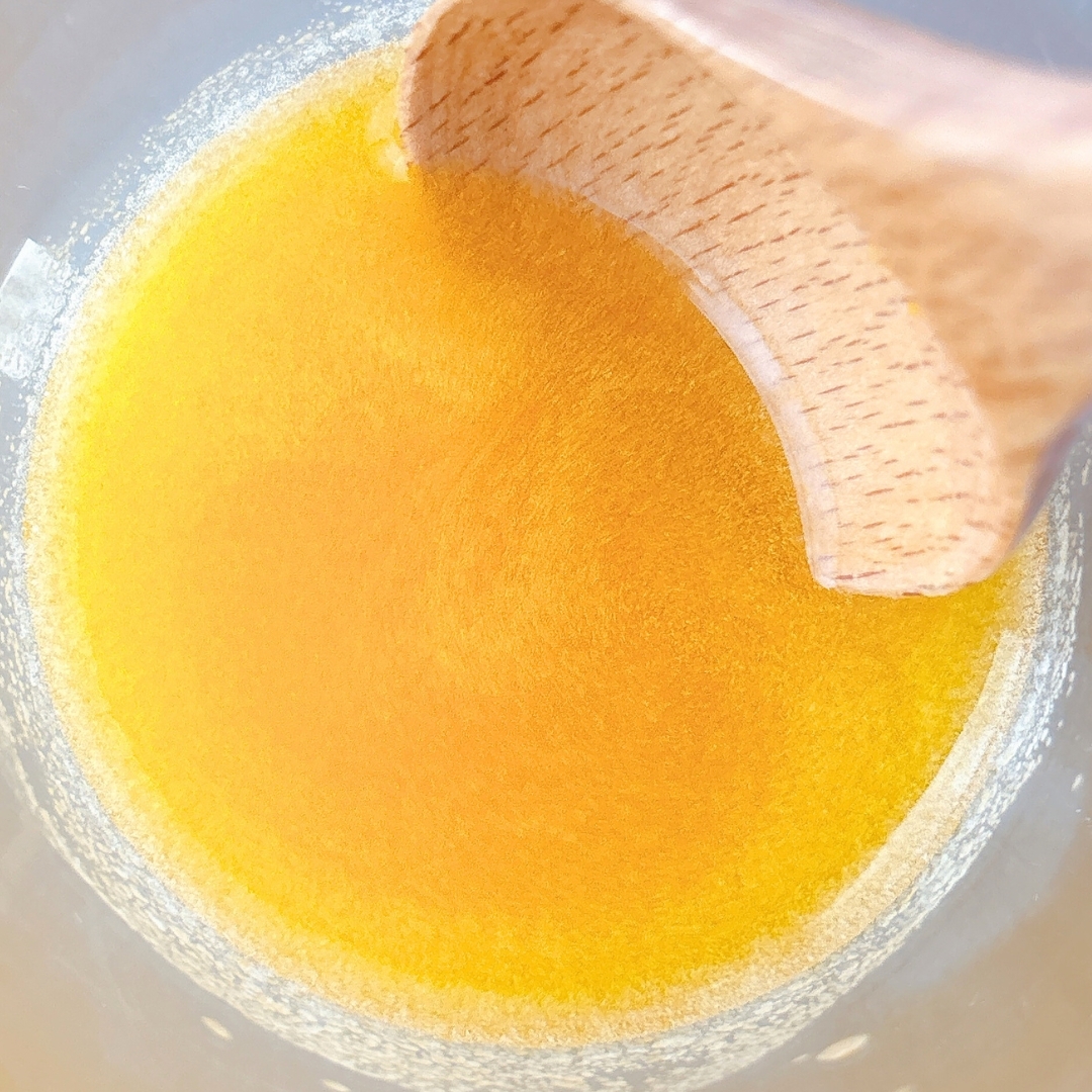 木のスプーンで混ぜられる鮮やかな黄色の液体がボウルに入っています。