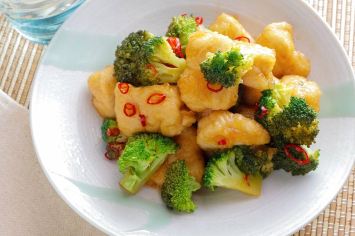 ブロッコリーと鶏のから揚げが皿に盛られ、赤唐辛子がトッピングされた料理。ガラスの水と緑の箸が横にある。