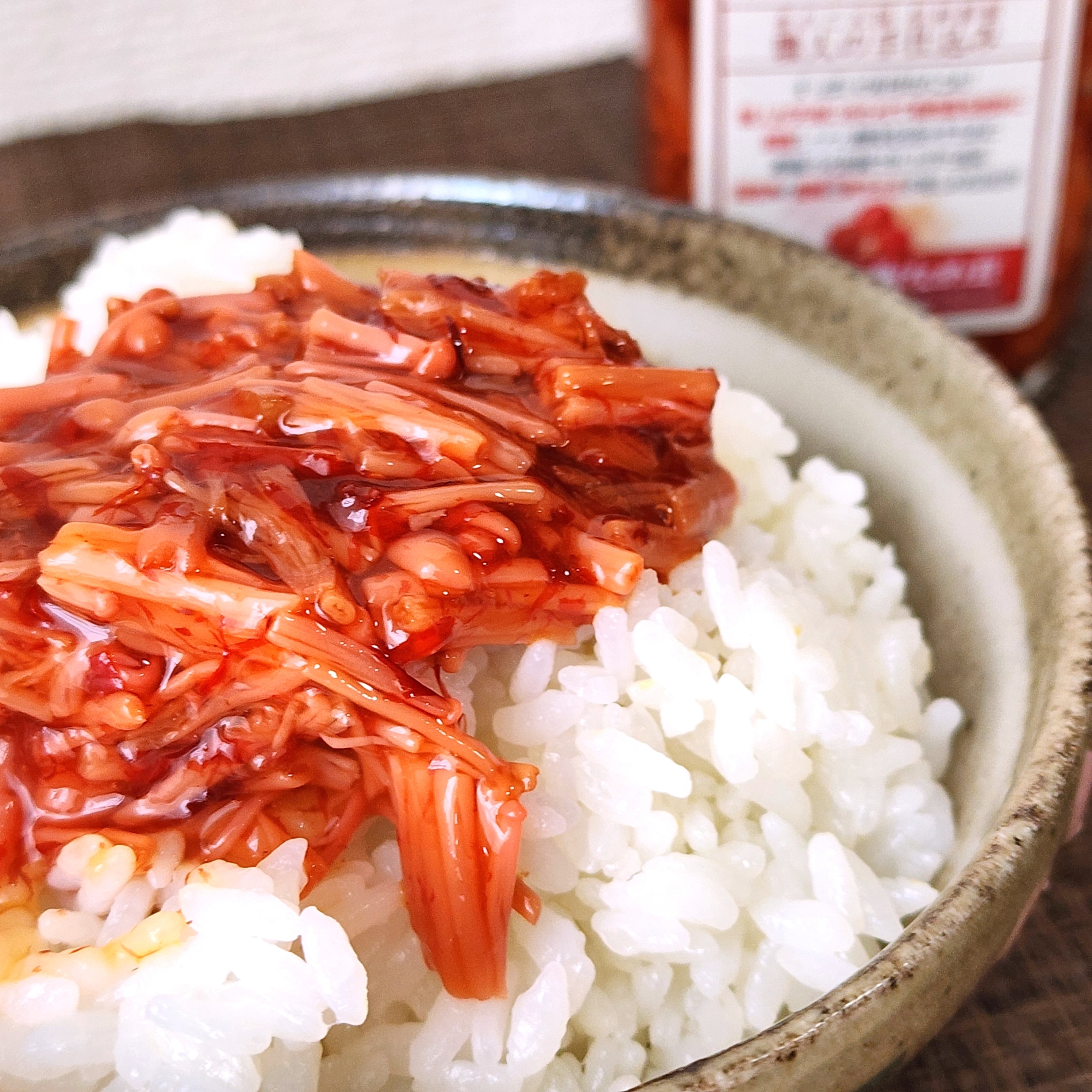 ご飯の上にエノキ茸の佃煮が載っている料理。背景に瓶入りの佃煮。