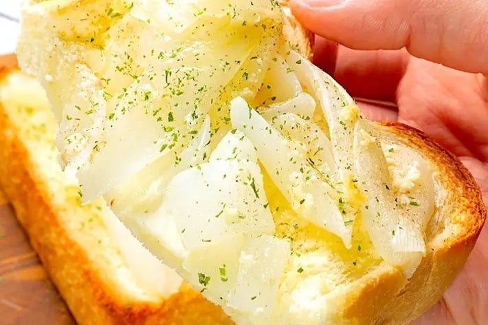 白いパンにスライスされた玉ねぎがのっているトーストが手に持たれている。