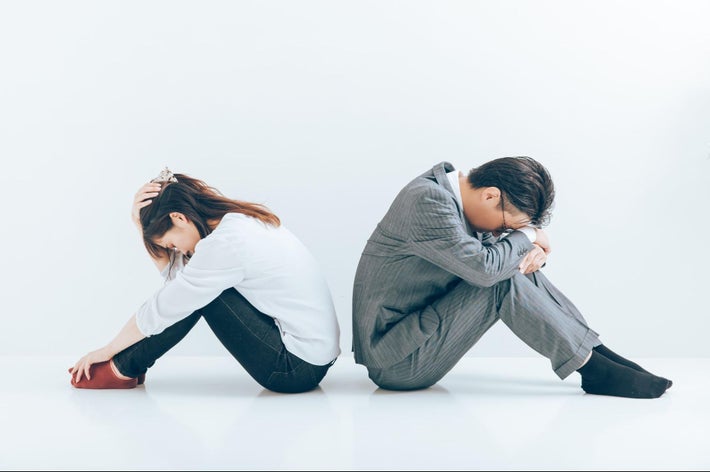 背中合わせに座り込むスーツ姿の男性とカジュアルな服装の女性。互いに考え込んでいる様子。