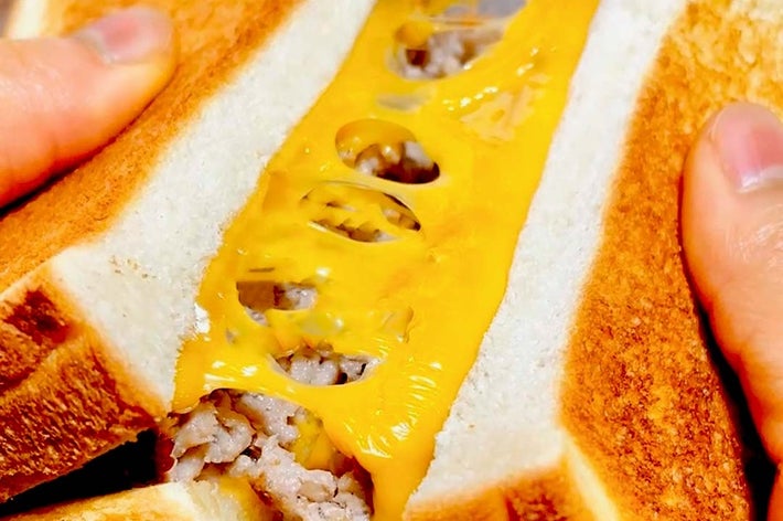 チーズをのせたトーストサンドイッチを手で持っている様子。中にはシンプルな具が入っている。
