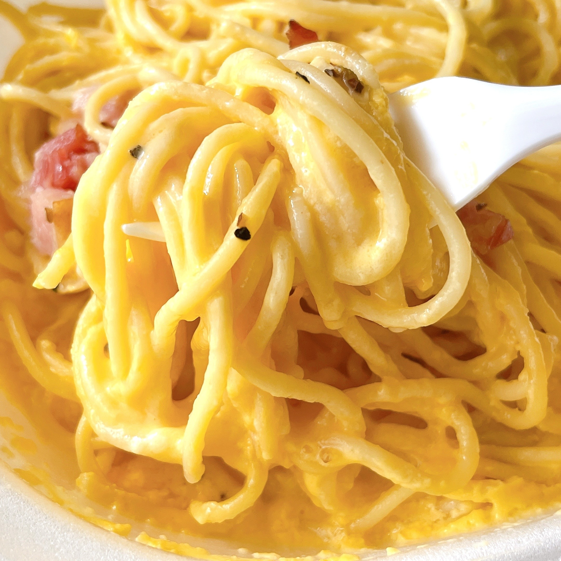 濃厚なカルボナーラのパスタをフォークで巻いている。クリーミーなソースとベーコンが見える。