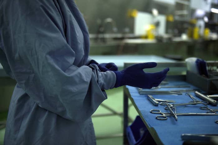 Person in surgical gown and gloves near medical instruments on a table, possibly preparing for a procedure in a clinical setting