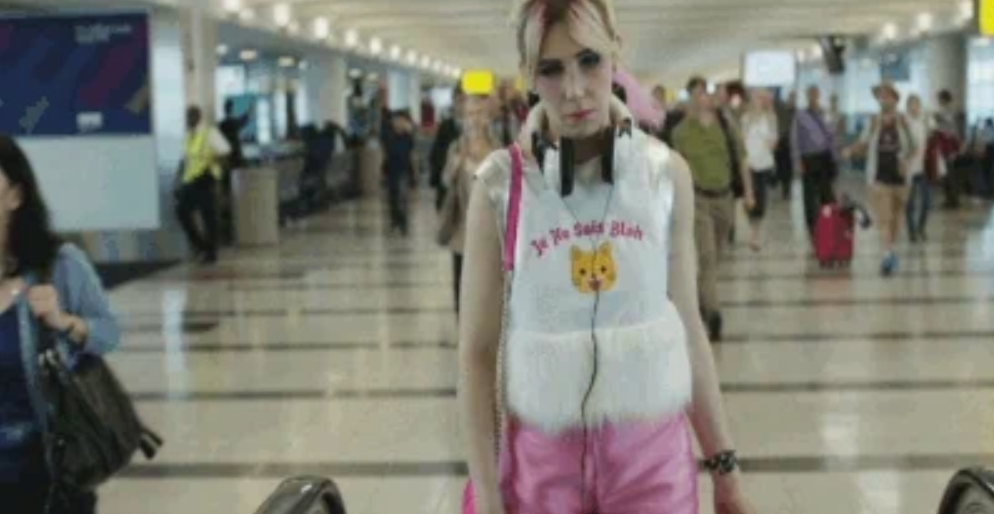 Person wearing a fluffy vest with a cat design and headphones, walking through an airport