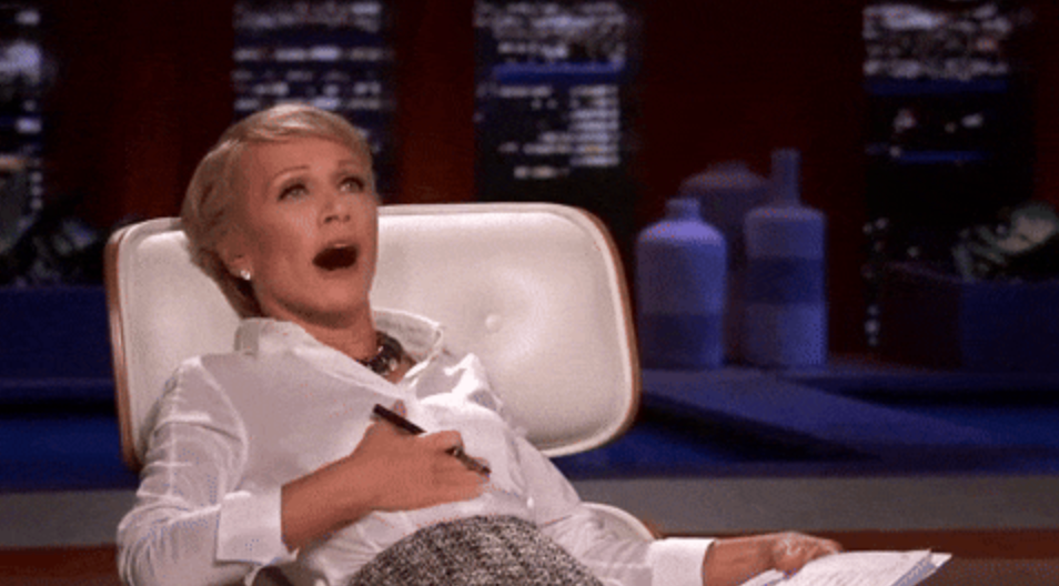 Person reclining in a chair, looking surprised, holding papers and a pen. They're wearing a white blouse and patterned skirt