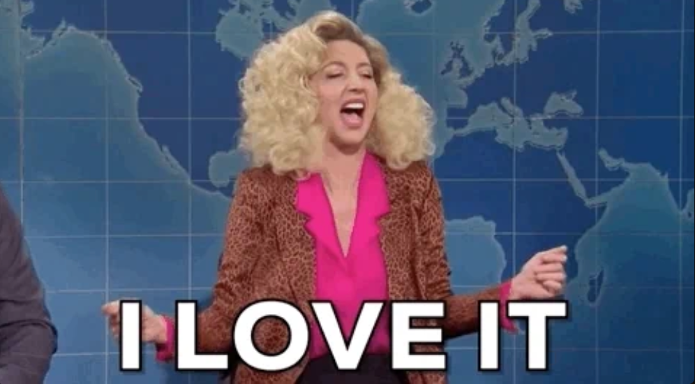 Person with curly hair enthusiastically gestures on a TV set with the words "I LOVE IT" displayed at the bottom