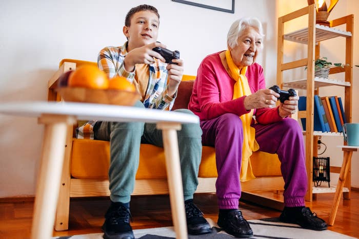 Older adult and boy sitting on a couch, playing video games with controllers, focusing intently