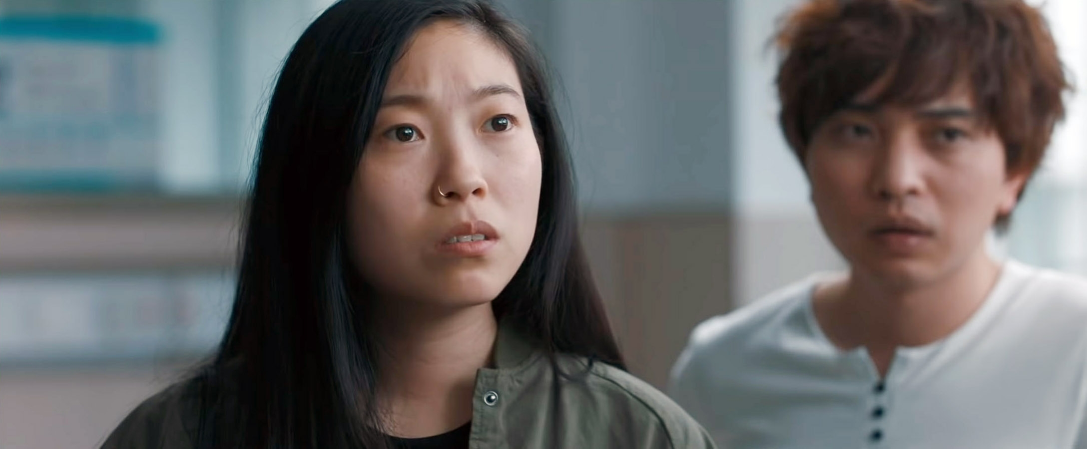 Two people look concerned in a scene from a TV show or movie. One has long, dark hair and the other has short hair