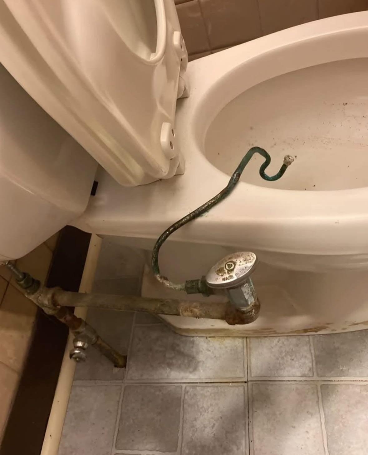 Unusual toilet with a bent pipe and a diverter valve attachment on its side, positioned over tiled flooring