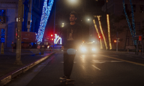 Person skateboarding down a city street at night with bright lights in the background