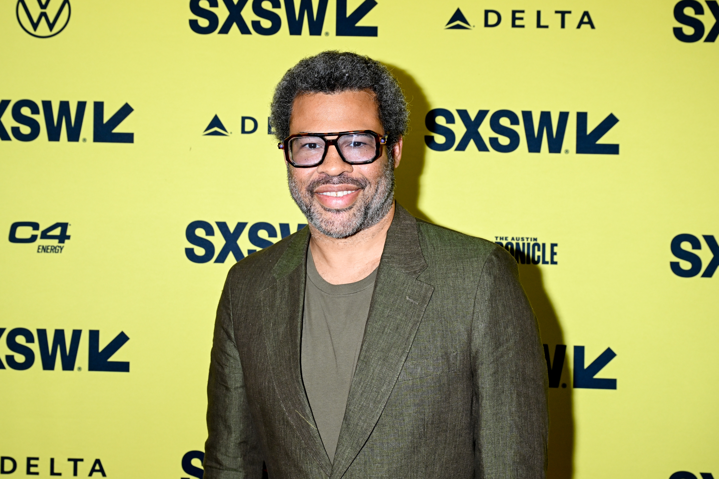 Jordan Peele in a tailored suit and t-shirt smiles at a SXSW event backdrop