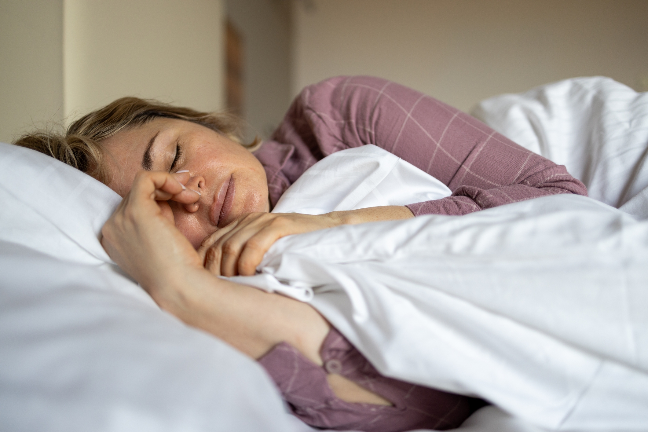 Person sleeping peacefully in bed, resting their head on a pillow, holding a blanket close