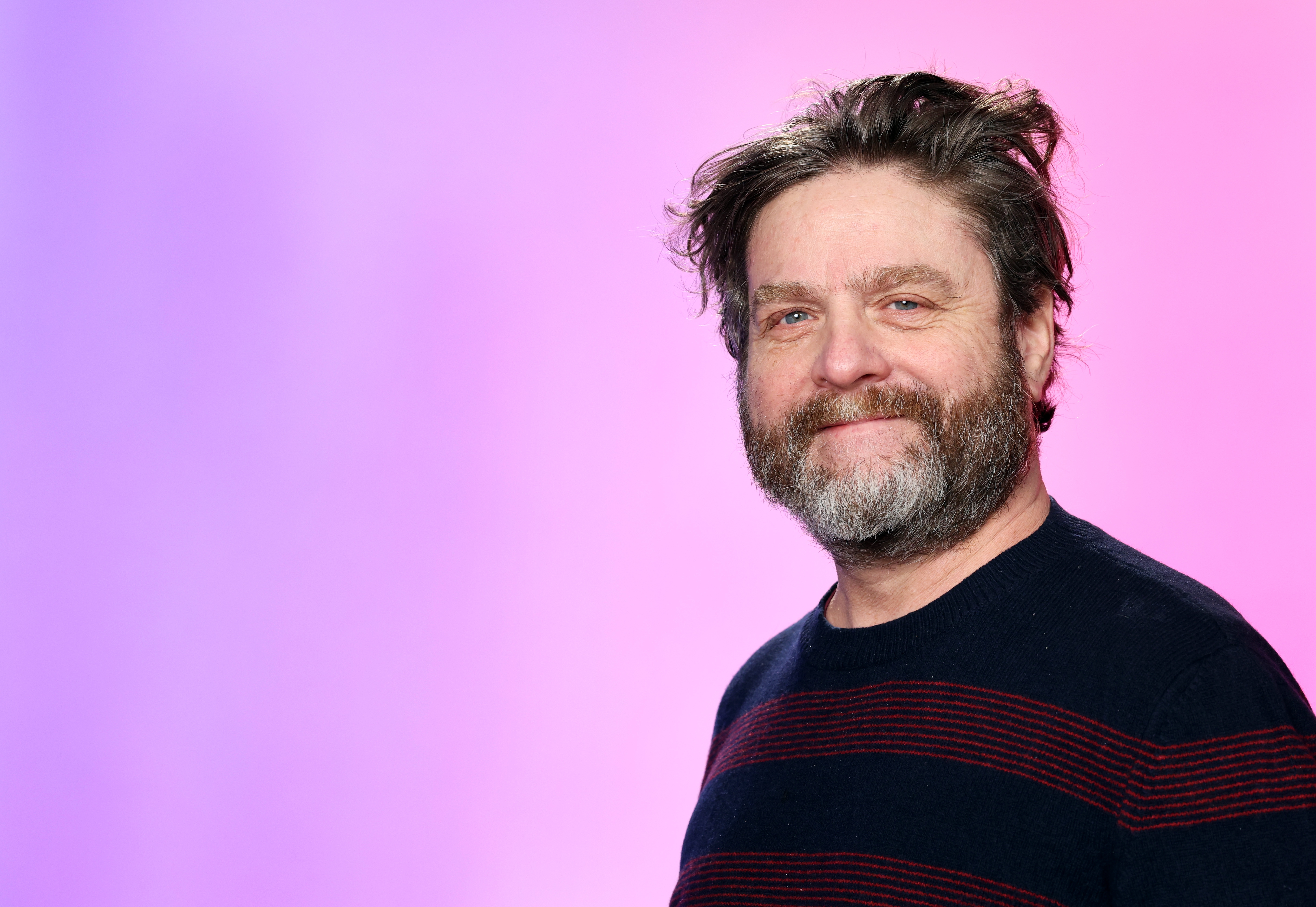 Zach Galifianakis poses against a pink and purple background
