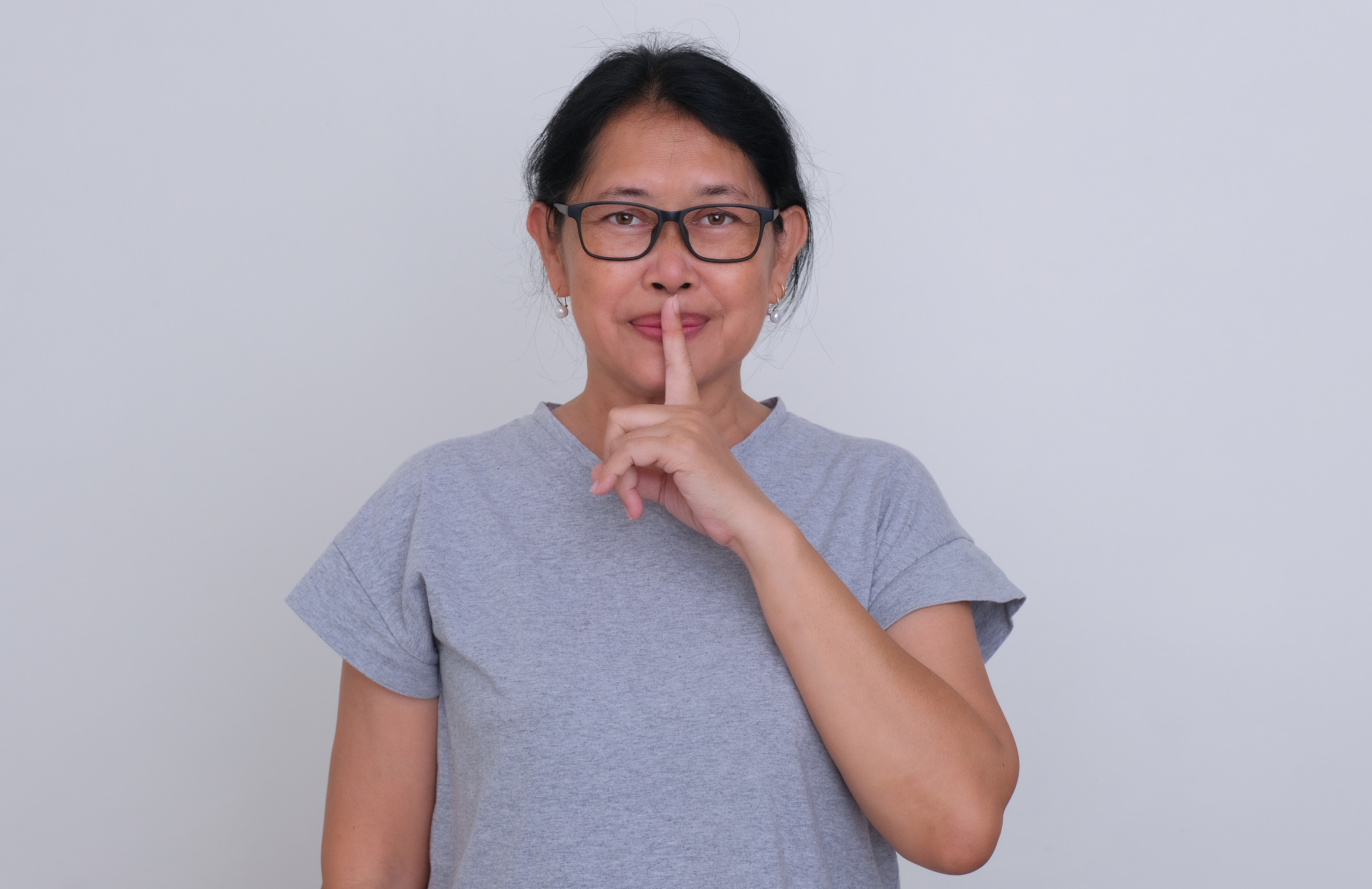 Person in a plain shirt holds a finger to their lips, gesturing for silence