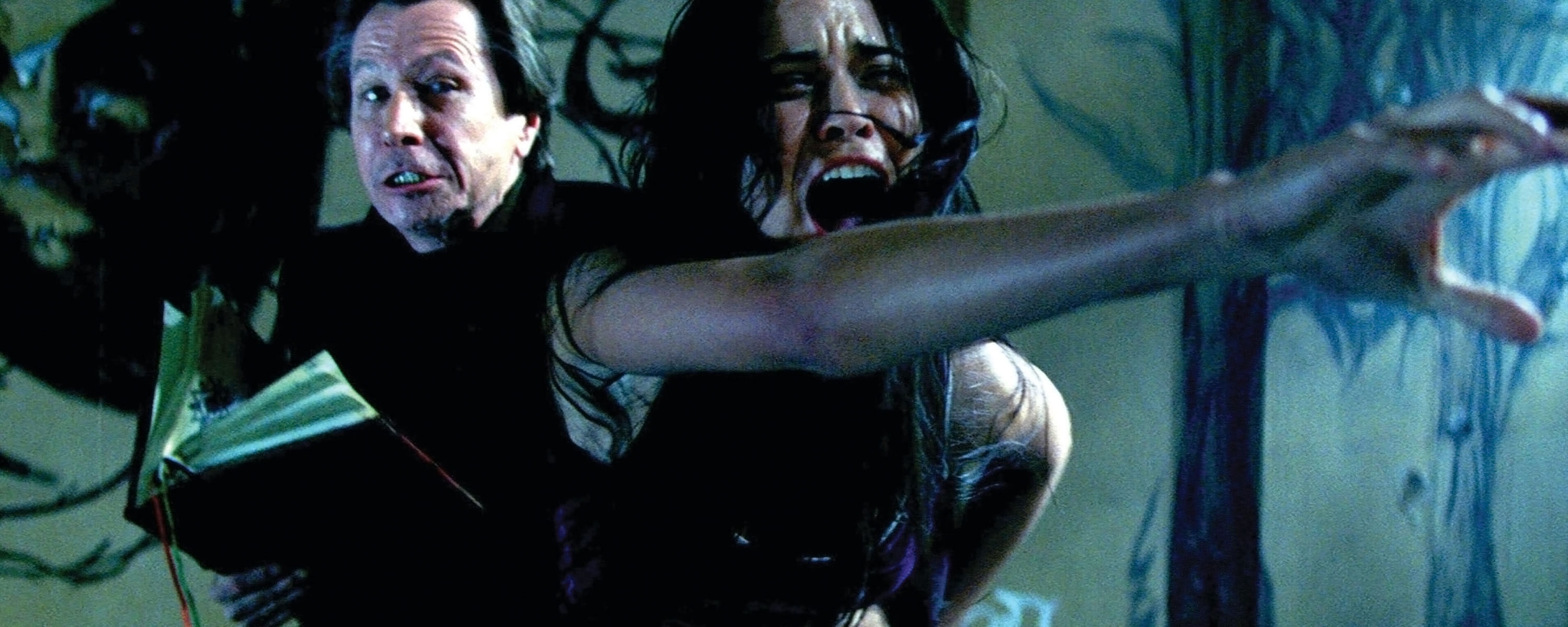 A person appears terrified, reaching out as another holds a book, in an intense scene, possibly from a suspense or horror film