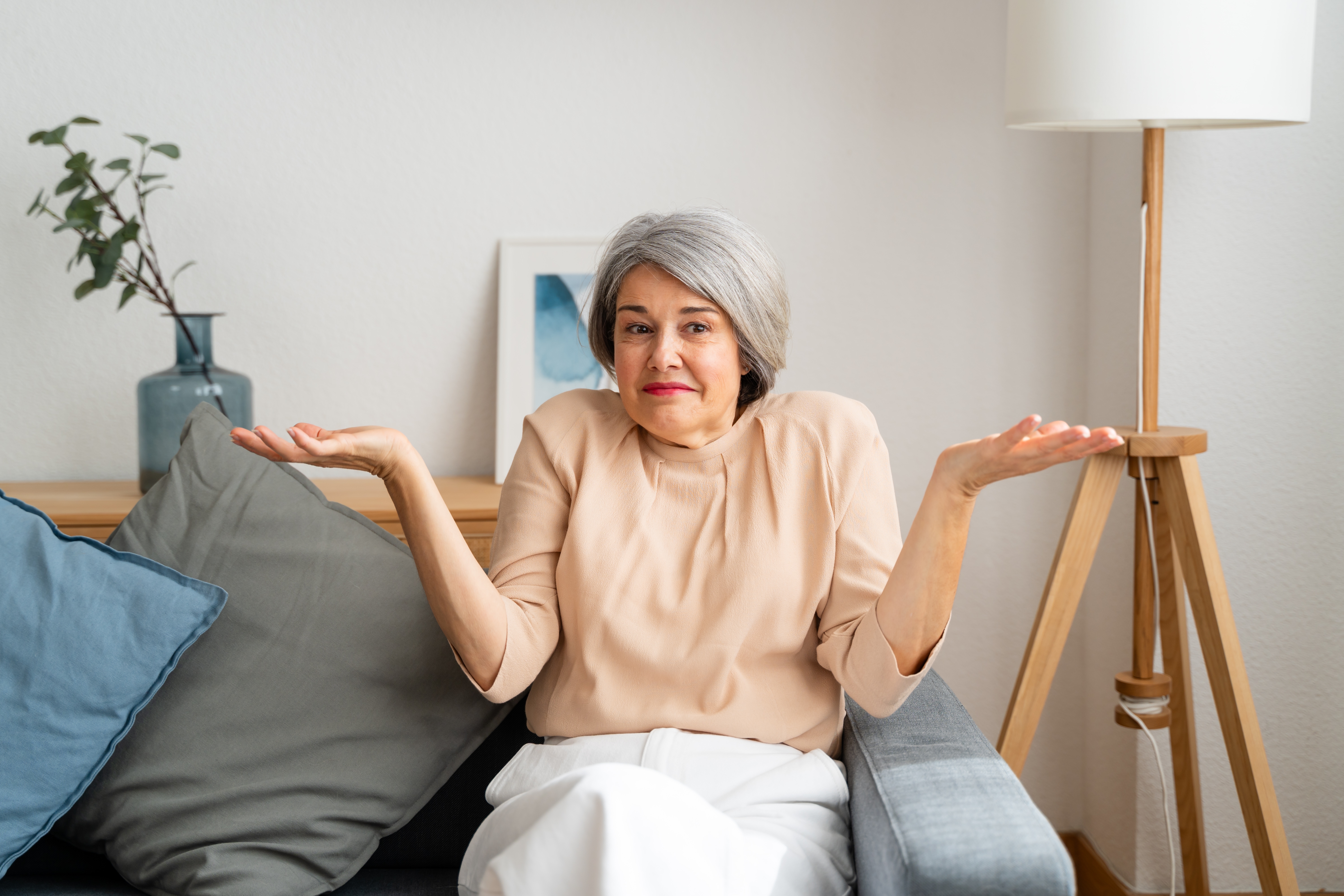 Person with short hair, sitting on a couch, shrugging with a puzzled expression. Comfortable, casual indoor setting