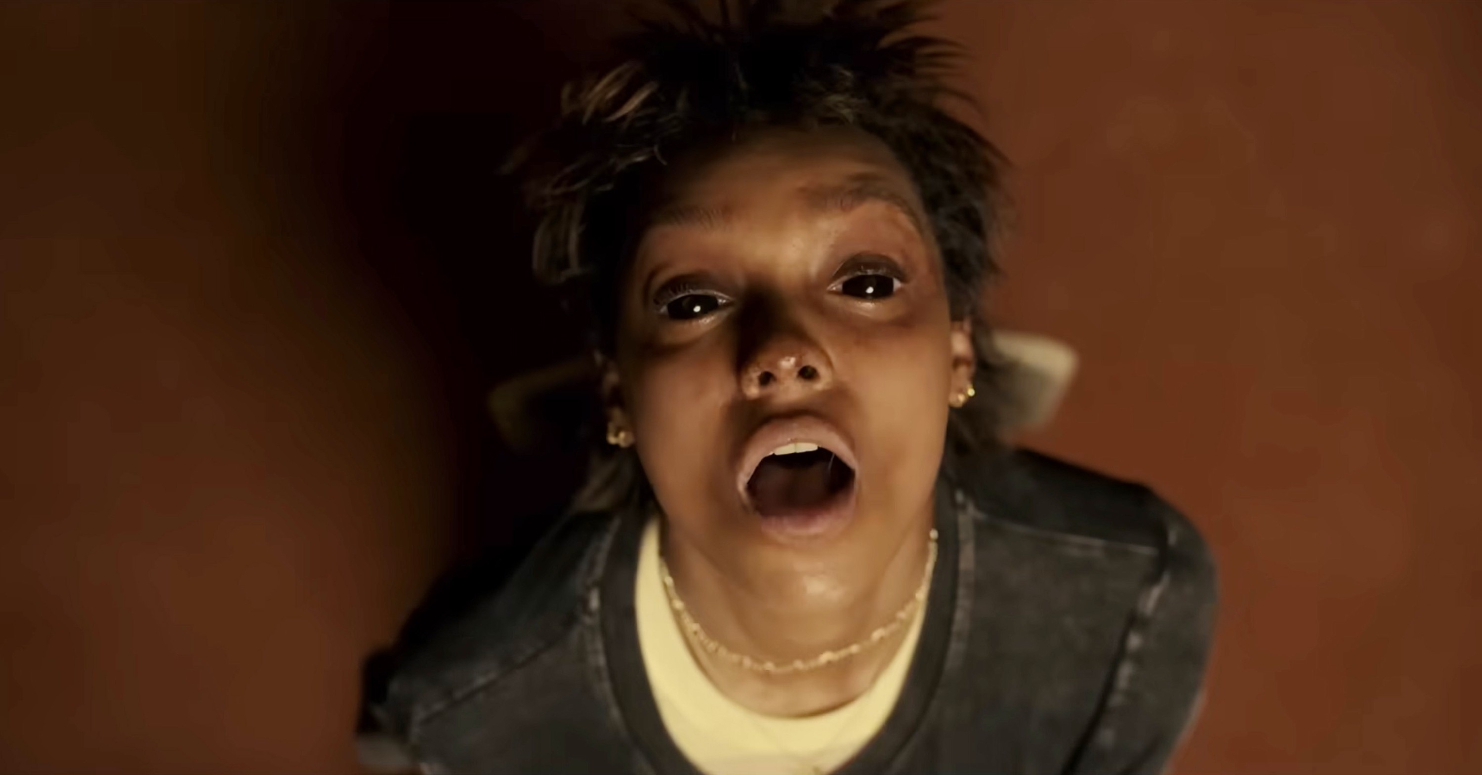 Person looking up with an open mouth, appearing startled or surprised. Casual attire includes a simple shirt and necklace