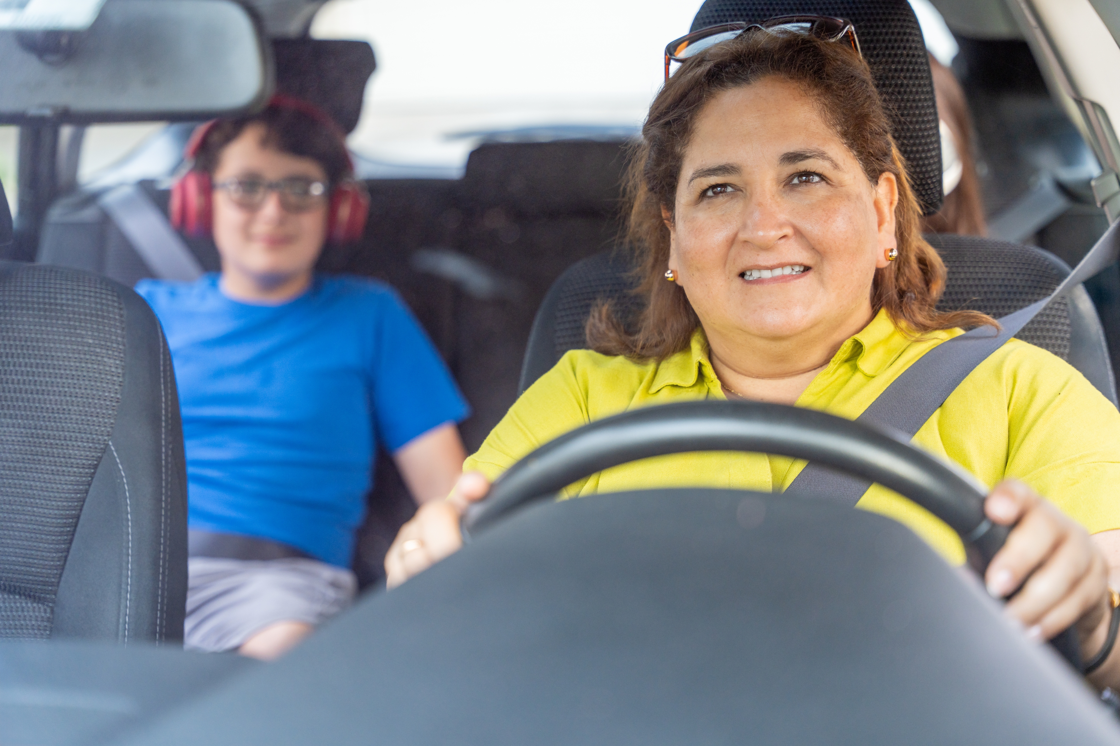 Woman driving a car with a child in the back seat wearing headphones