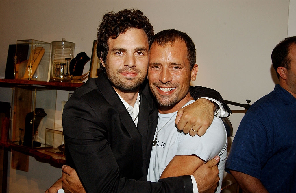 Two people hugging at an event. One wears a suit, the other a casual T-shirt. Smiling, friendly atmosphere