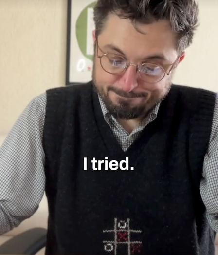 Person wearing glasses with a checkered shirt and vest, looking down with a slight smile. Text on image reads: "I tried."