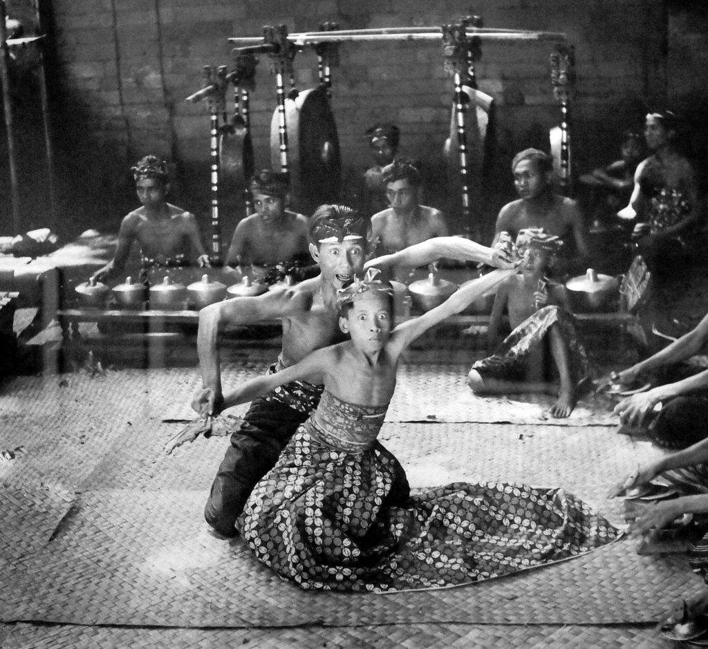 Traditional Balinese dancers perform in a seated position, surrounded by musicians playing gamelan instruments