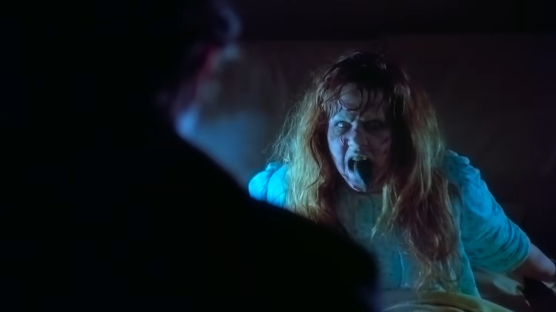 A person with disheveled hair and an intense expression is yelling at someone in a dimly lit setting, creating a dramatic scene