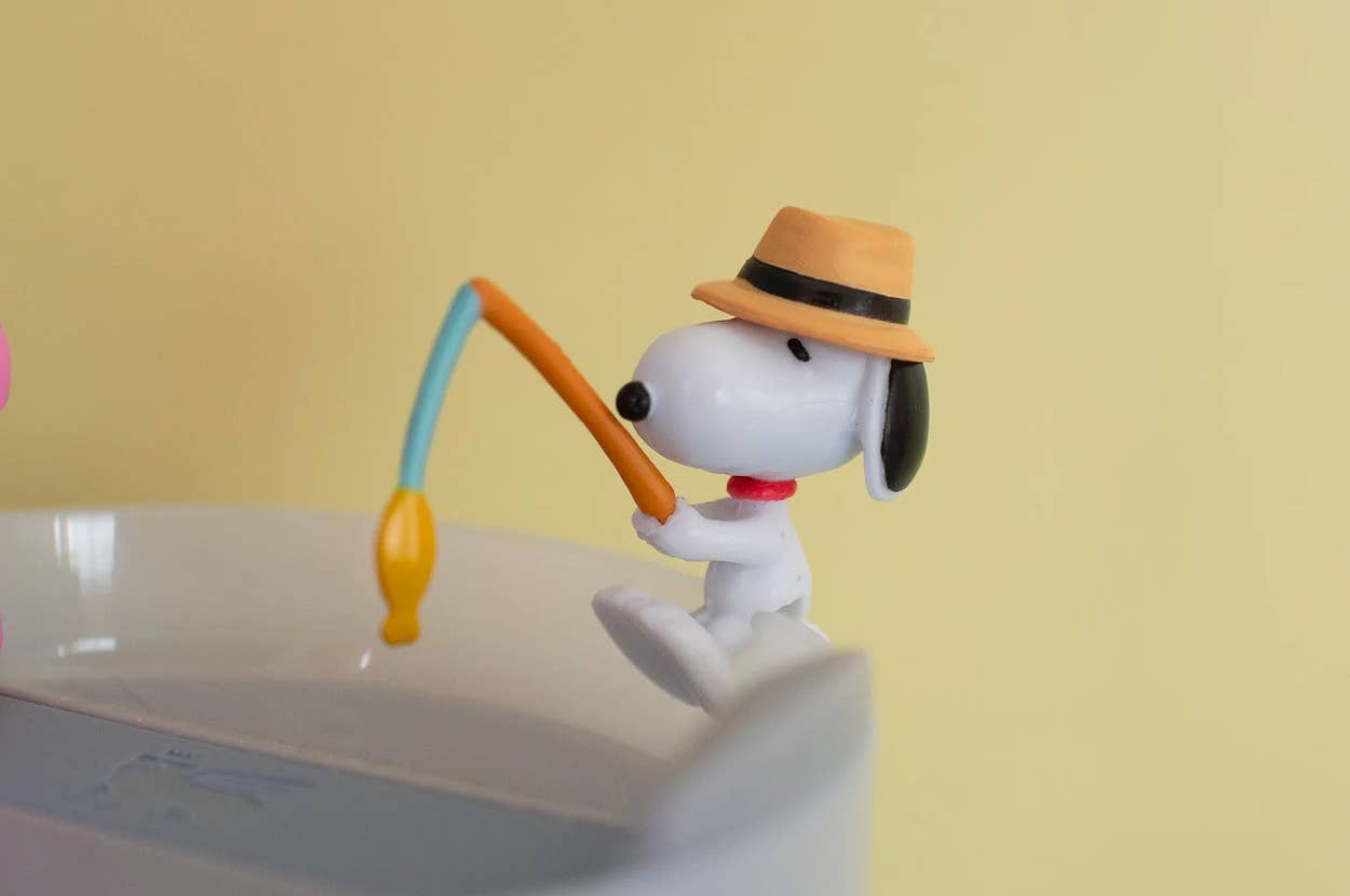 Toy dog figurine with a hat fishing on the edge of a cup against a plain background