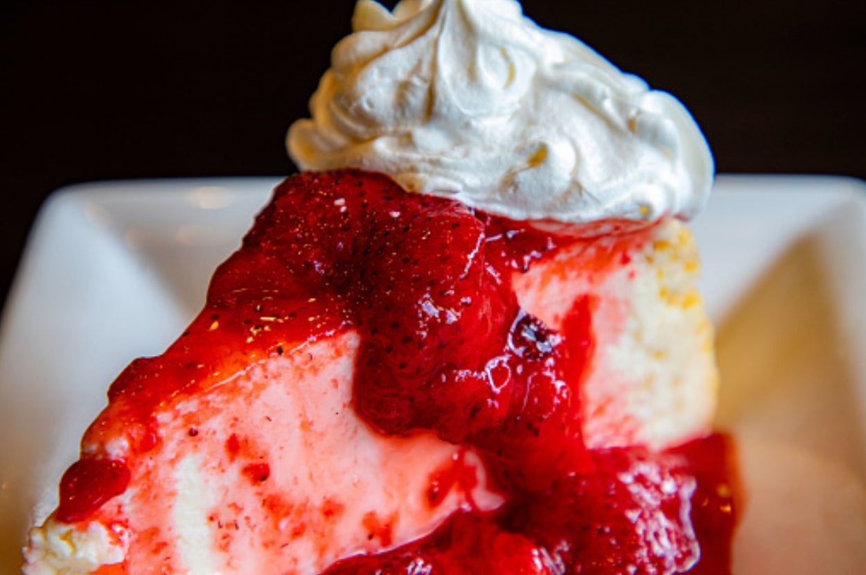 Slice of cheesecake topped with strawberry sauce and whipped cream on a plate