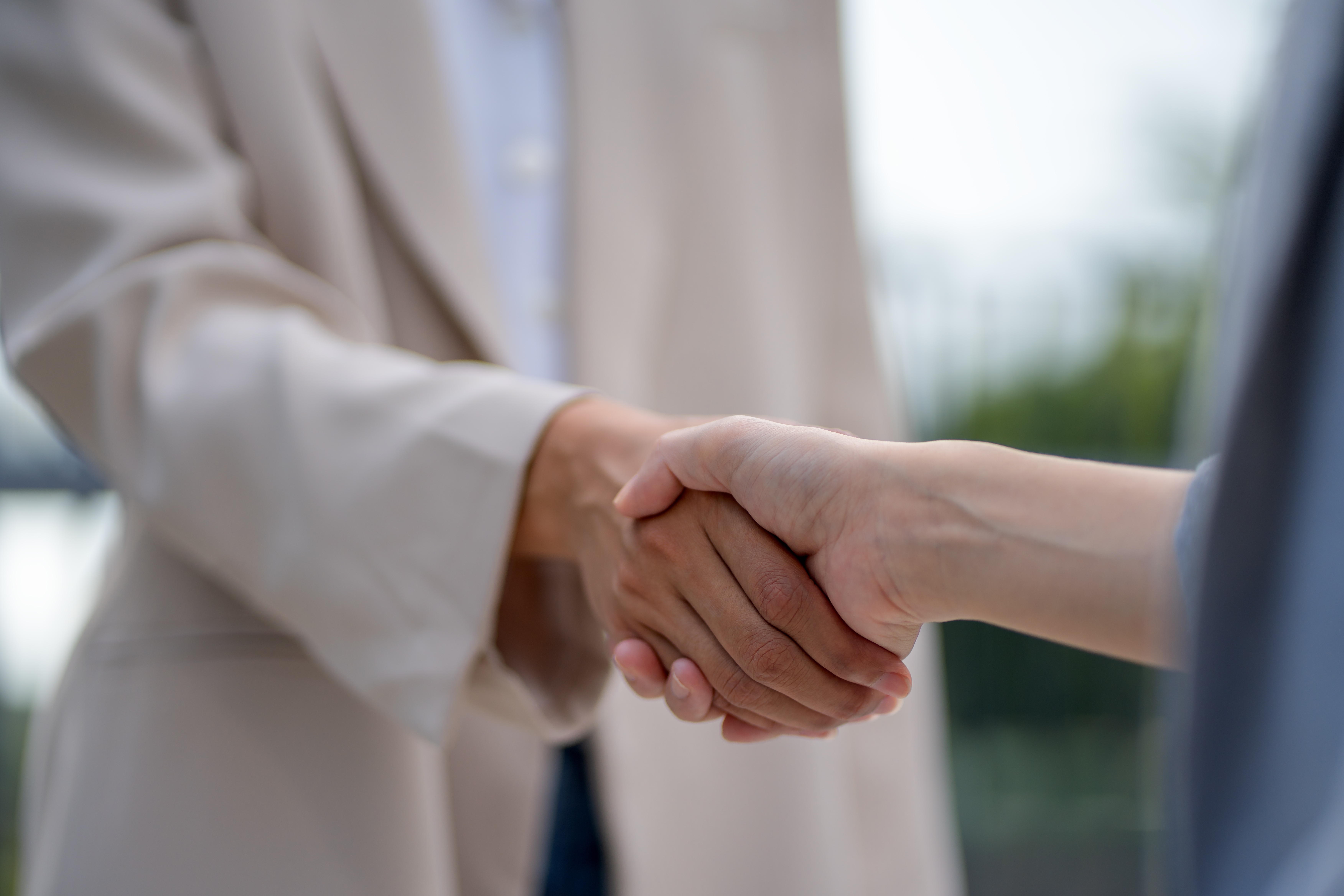 Two people shaking hands, one wearing a light-colored suit jacket, symbolizing agreement or partnership