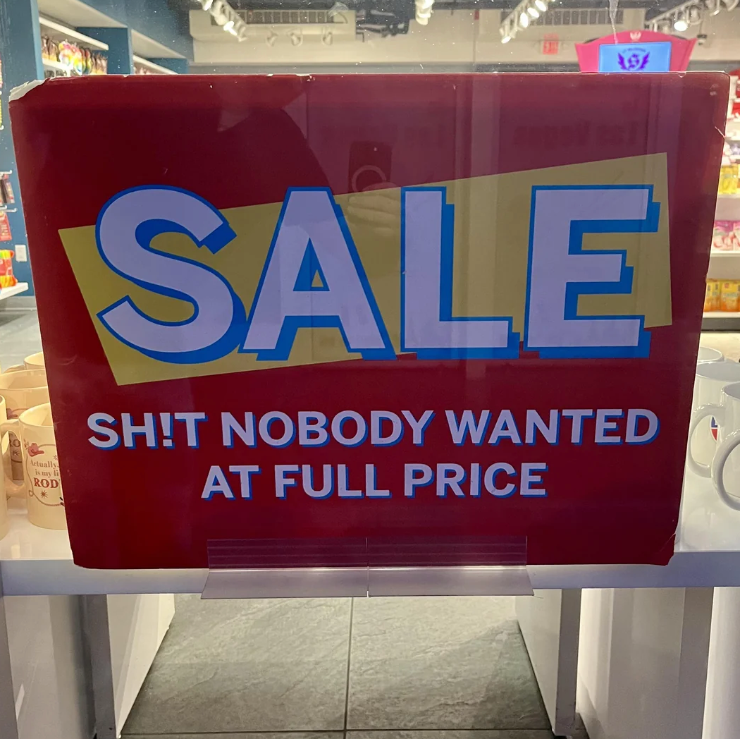 Sign in store window humorously reads: "SALE SH!T NOBODY WANTED AT FULL PRICE."