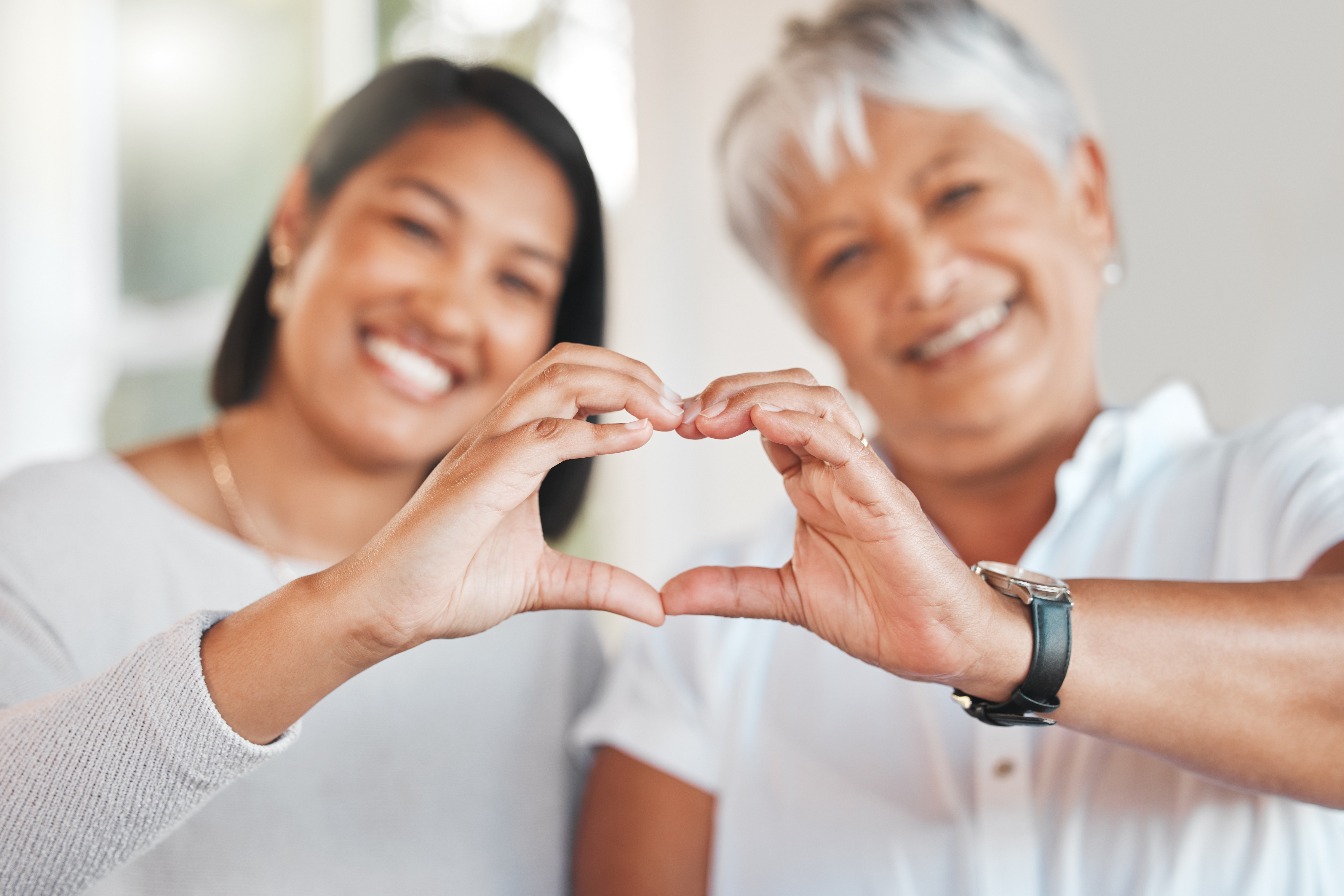 Two smiling people, making a heart shape with their hands, showcasing affection and togetherness