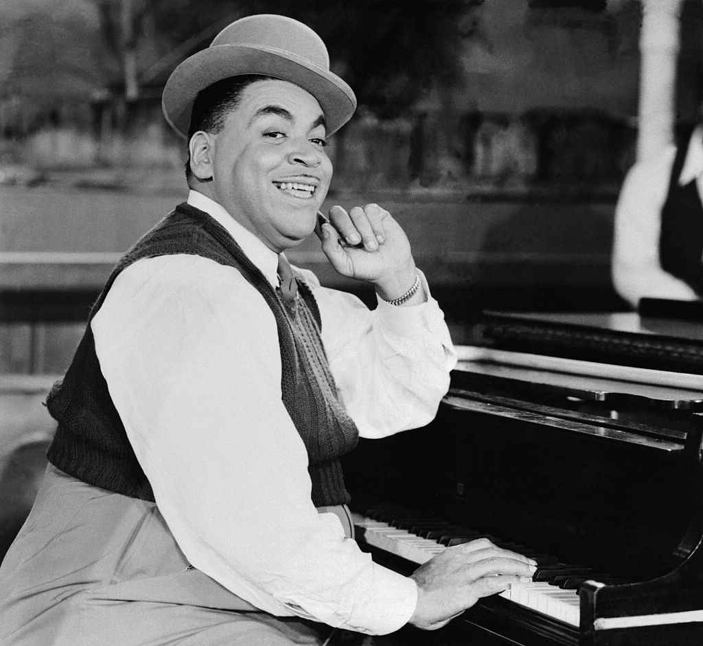 Person in vintage attire, wearing a bowler hat, smiling while playing a piano