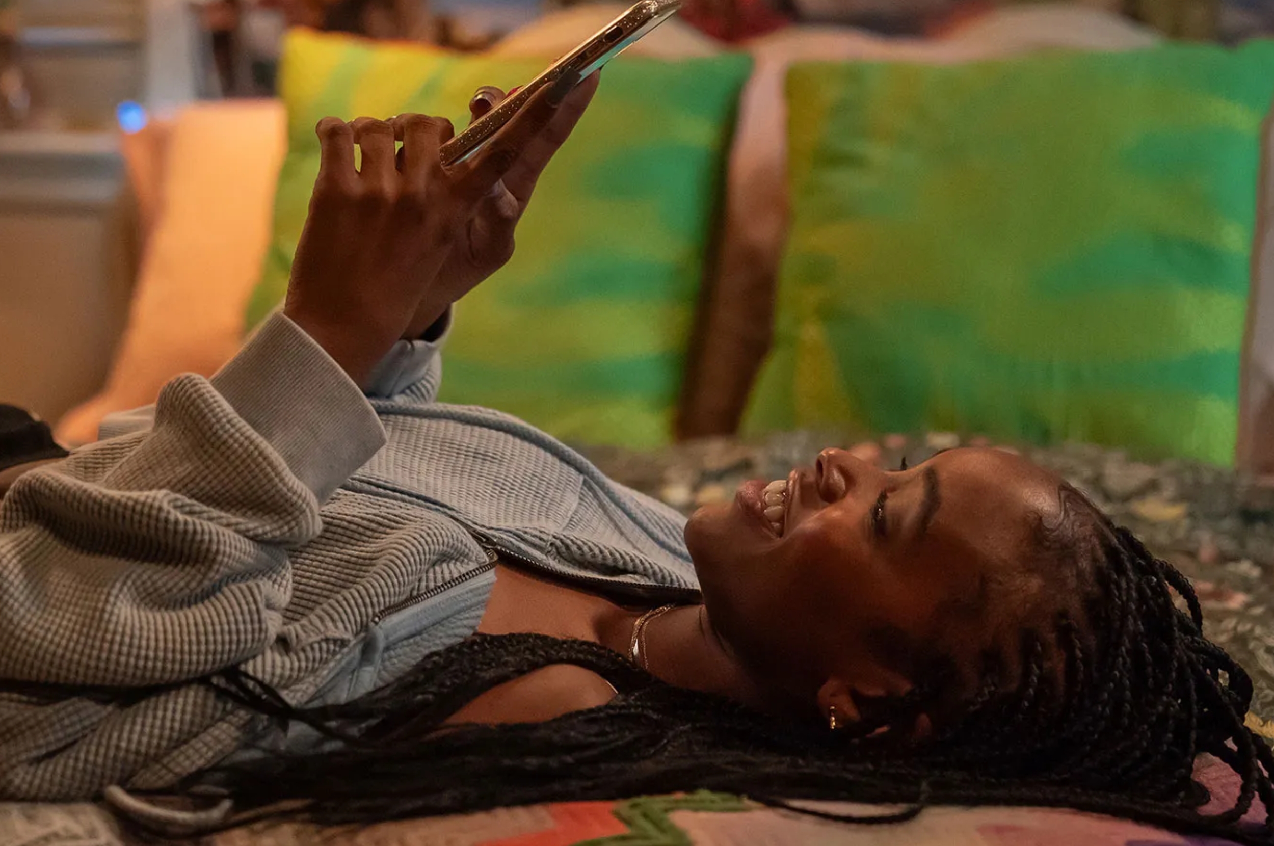 Person lying on a bed, smiling at a phone. Casual setting, cozy attire