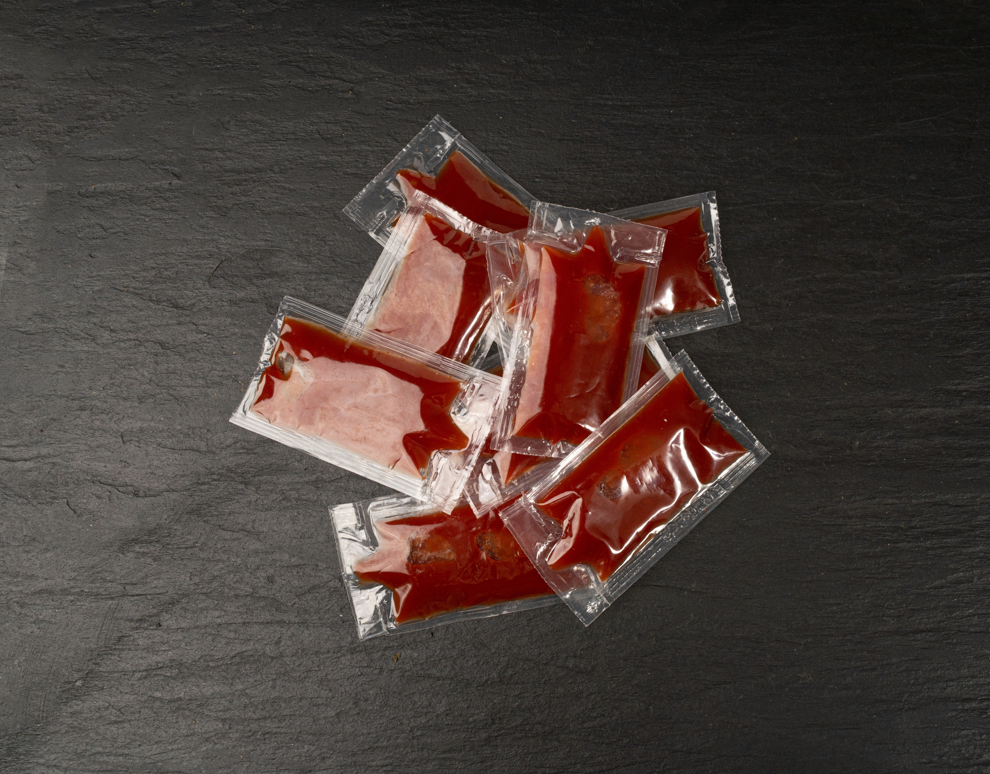 Several ketchup packets spread on a dark surface