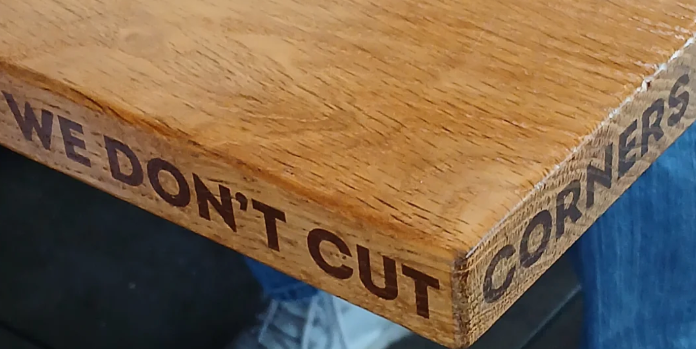 Wooden table edge with engraved words: "WE DON'T CUT CORNERS."