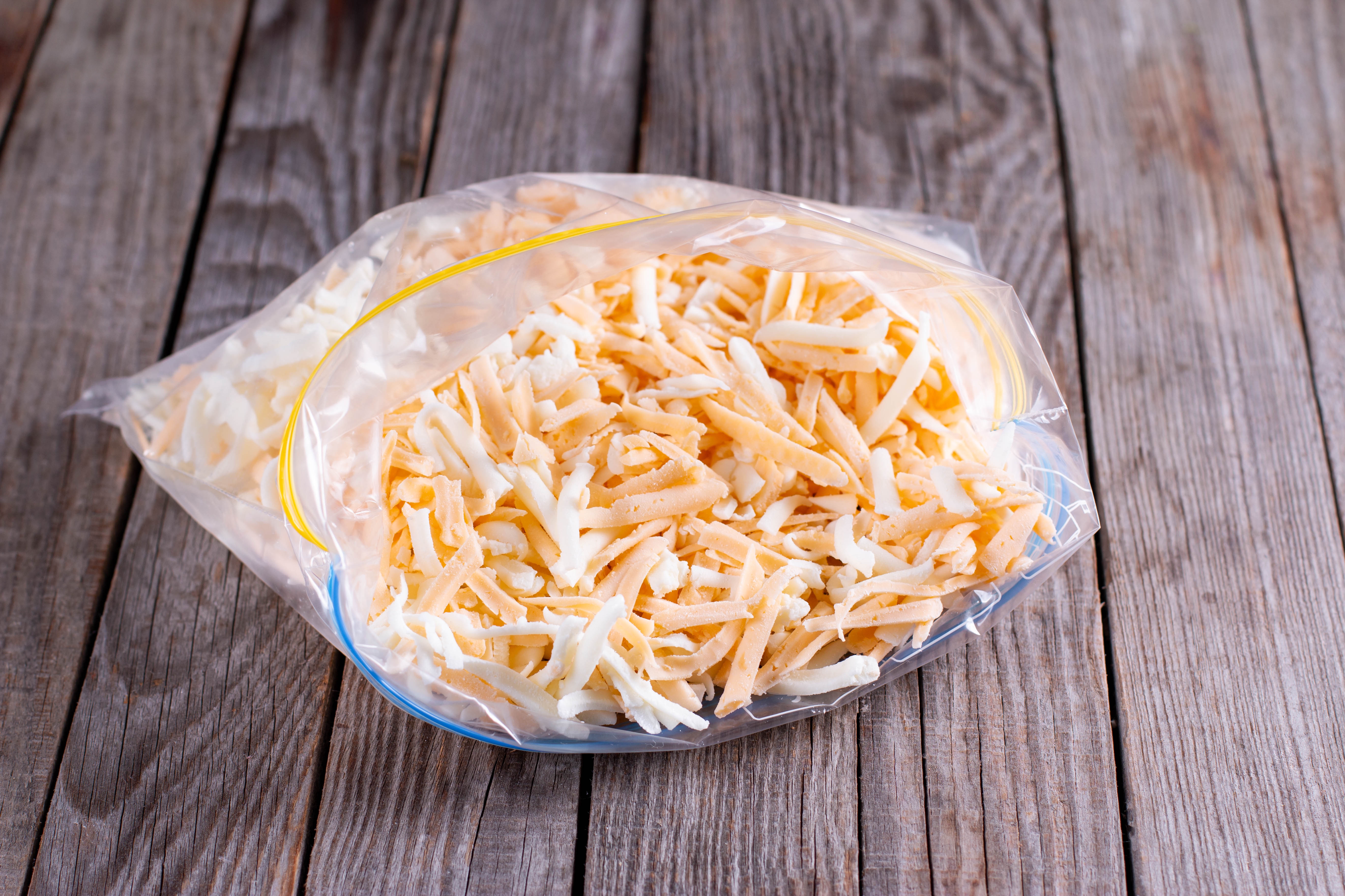 Shredded cheese in a clear resealable plastic bag on a wooden surface
