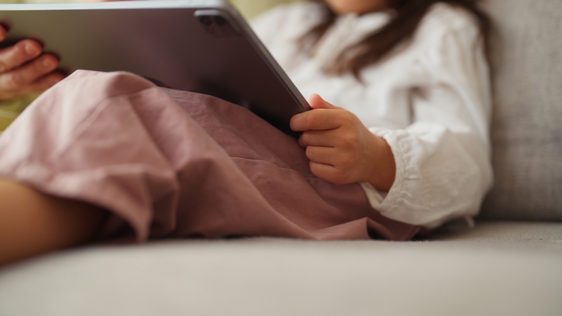 Child sitting on a couch, holding a tablet, partially visible
