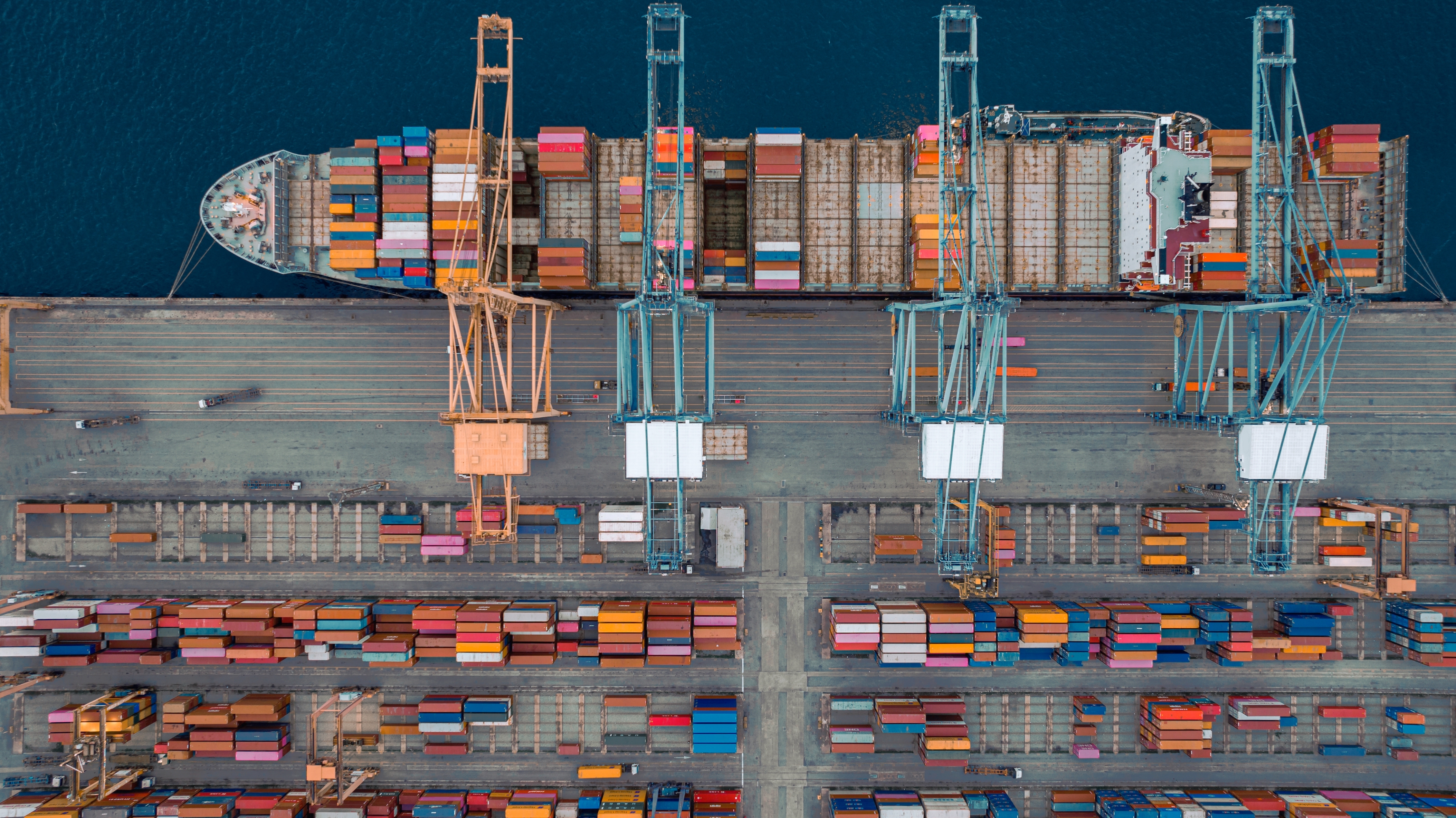 Aerial view of a bustling shipping port with cranes and stacked cargo containers on ships and docks, highlighting global trade