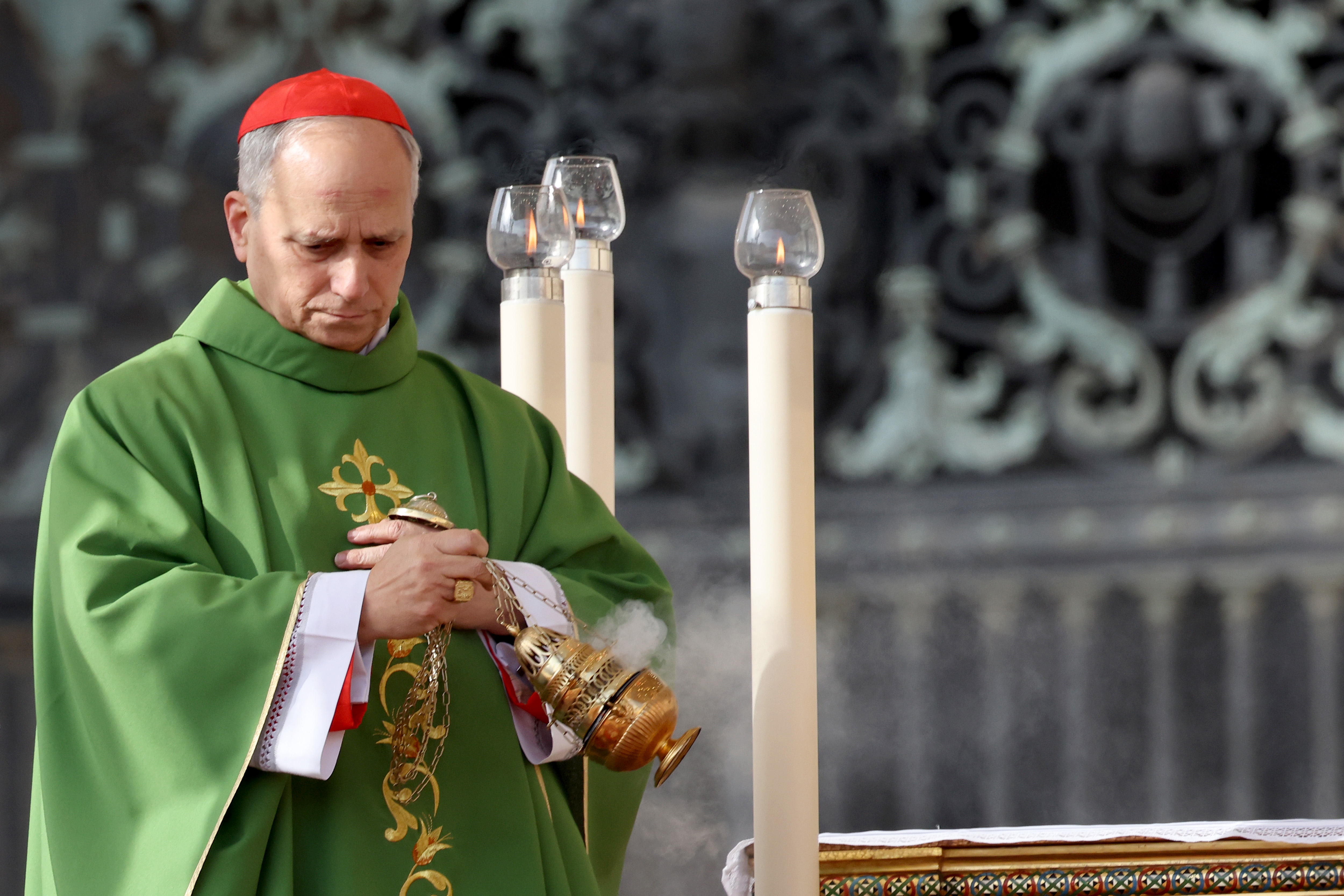 A religious figure in a ceremonial green robe holds an incense burner, participating in a formal religious ceremony