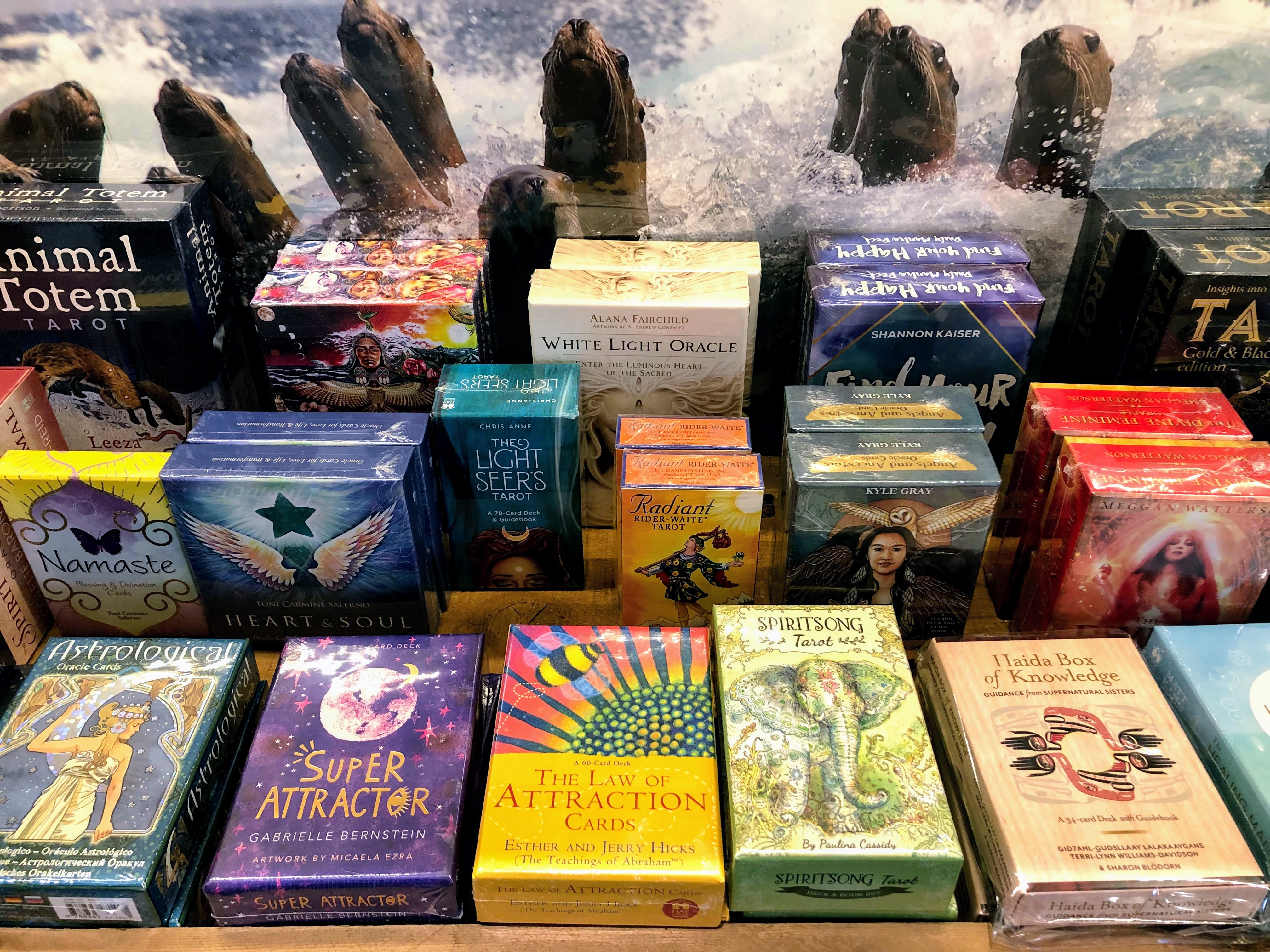 Shelf displaying various oracle and tarot card decks with colorful designs, including "Light Seers Tarot" and "The Law of Attraction Cards."
