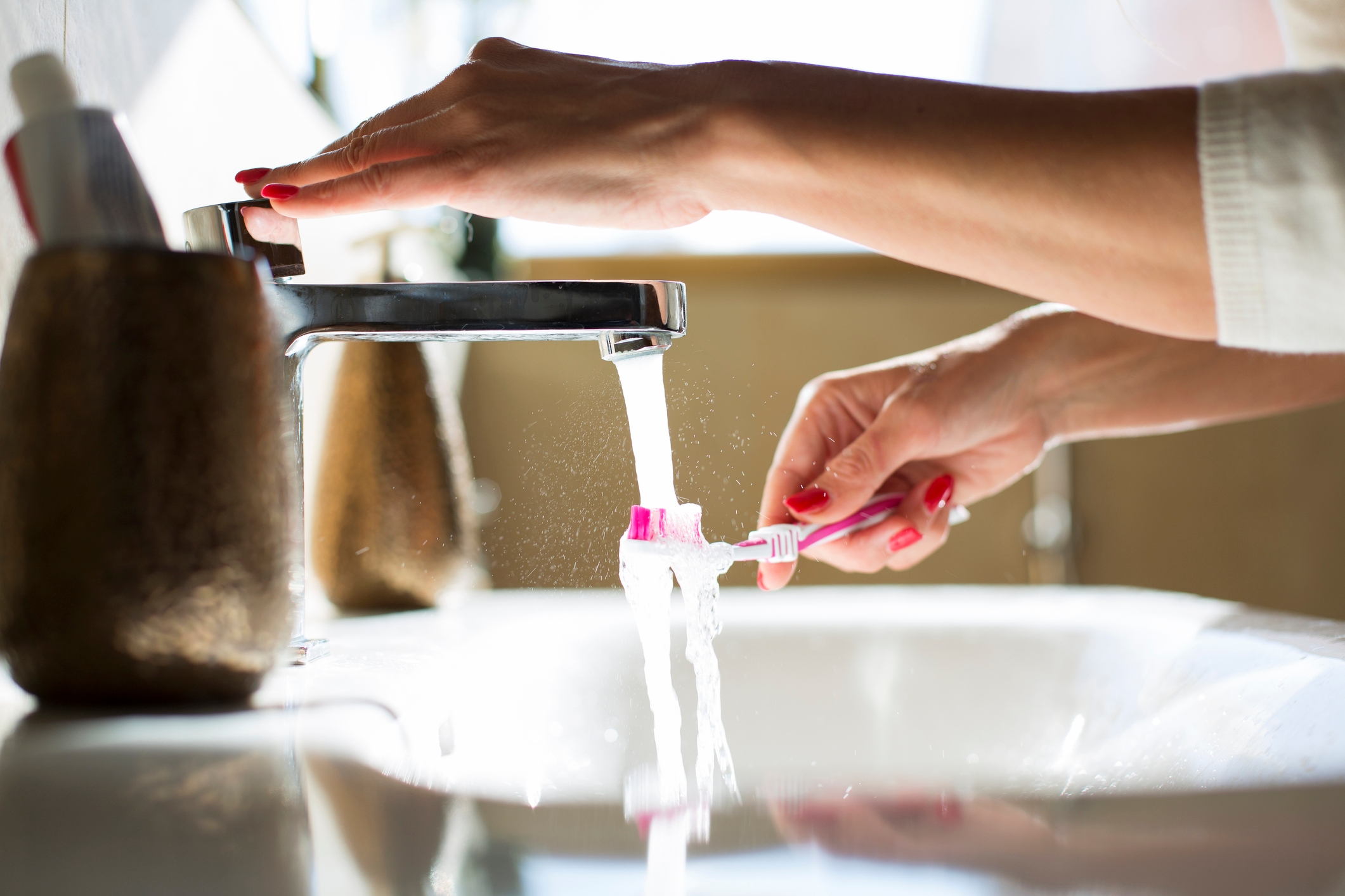 Person rinsing a toothbrush under running water in a bathroom sink