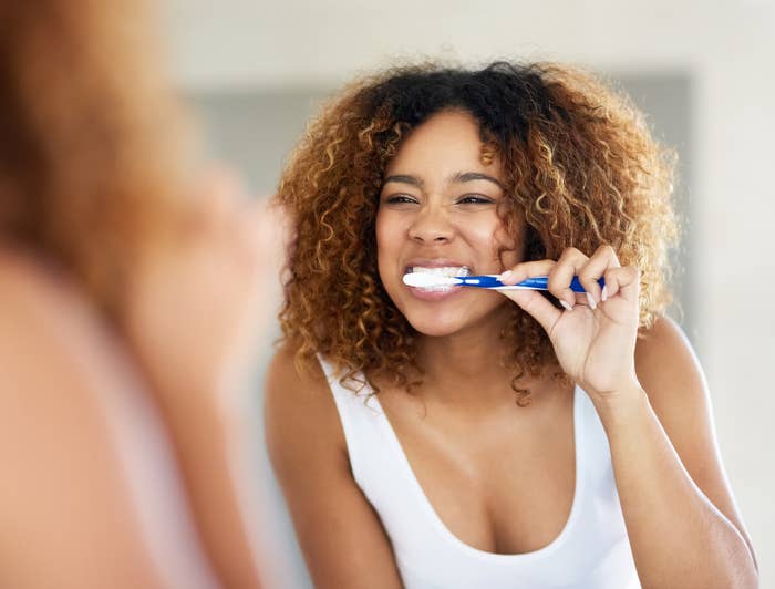 Person smiling while brushing teeth in front of a mirror