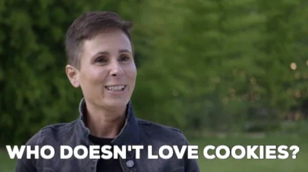 Person with short hair smiles outdoors. Text on image reads, "Who doesn't love cookies?"