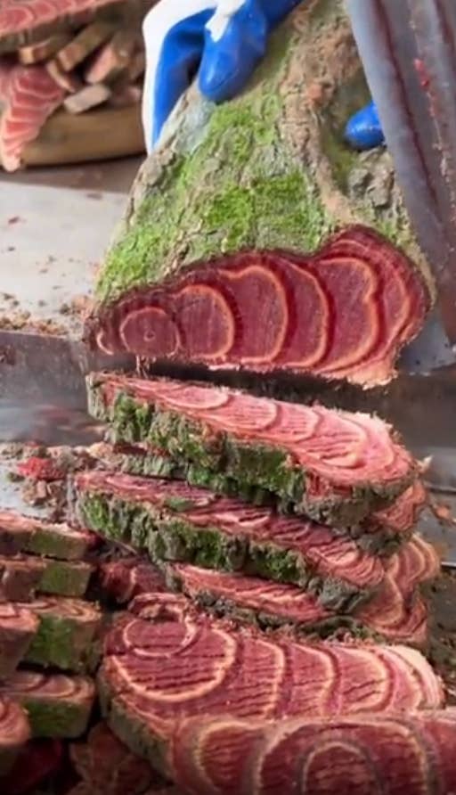 A person slices wood with a unique pink and green pattern, resembling the texture of cooked meat