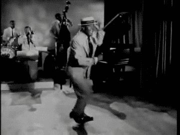 A performer energetically tap dances in a vintage setting, accompanied by a jazz band in the background