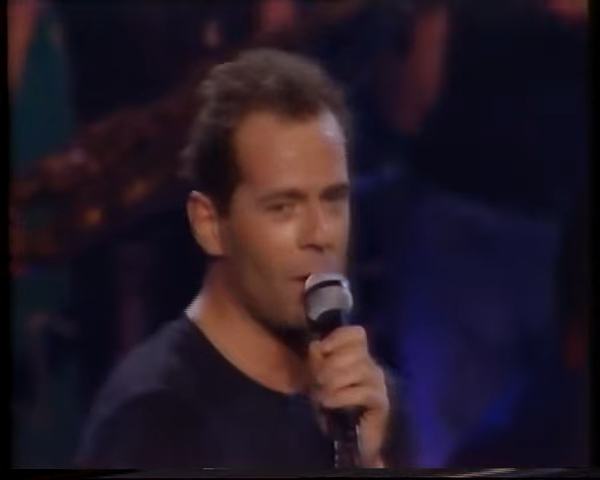 Person holding a microphone on stage, mid-performance, wearing a dark shirt