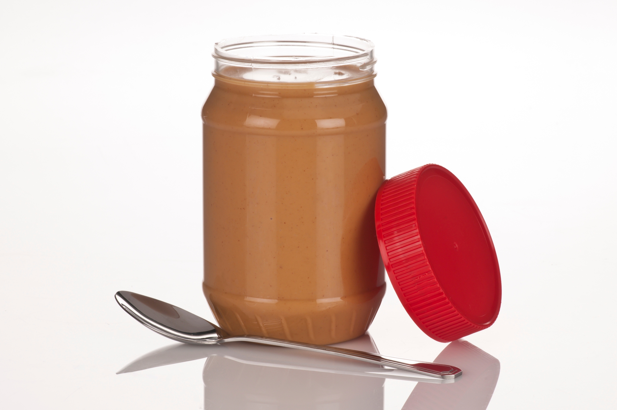 Open jar of peanut butter with a spoon beside it on a white background